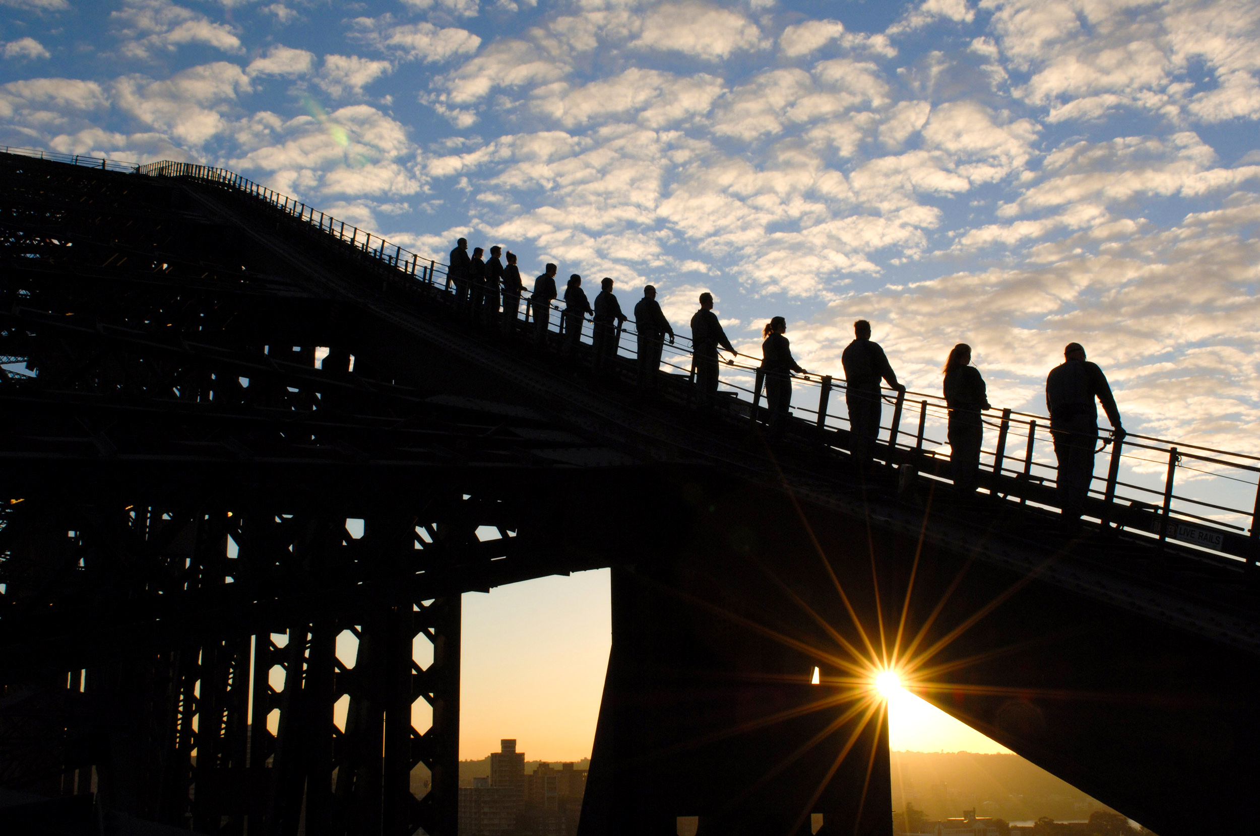 people standing on the top arch of the sydney harbour bridge at dawn