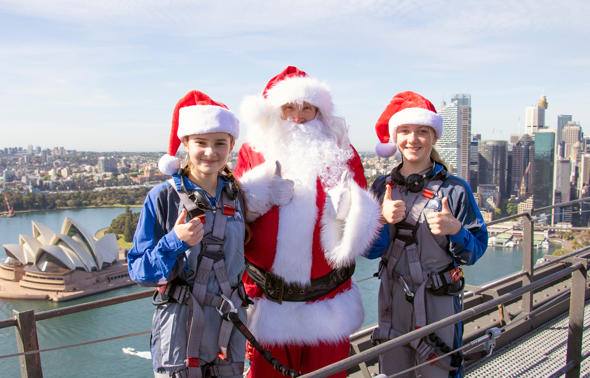 Santa Claus standing at the summit of the sydney harbour bridge giving a young boy a high five for a BridgeClimb santa photo