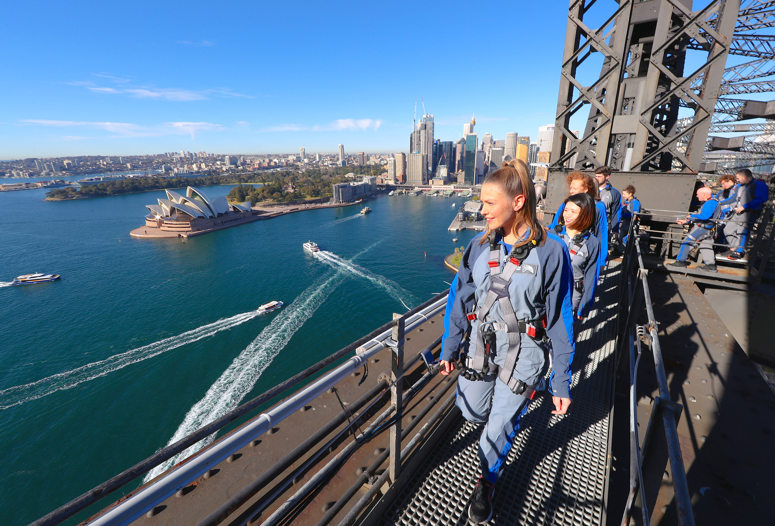 group of climbers on the lower arch of the sydney harbour bridge with a view of the harbour and sydney opera house in the background