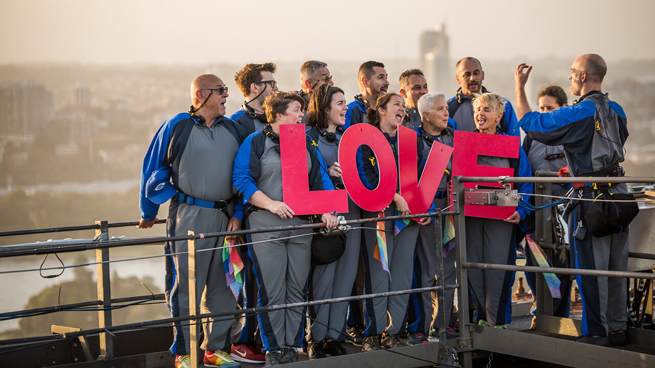 group of bridgeclimbers at the summit posing for a photo holding the word love
