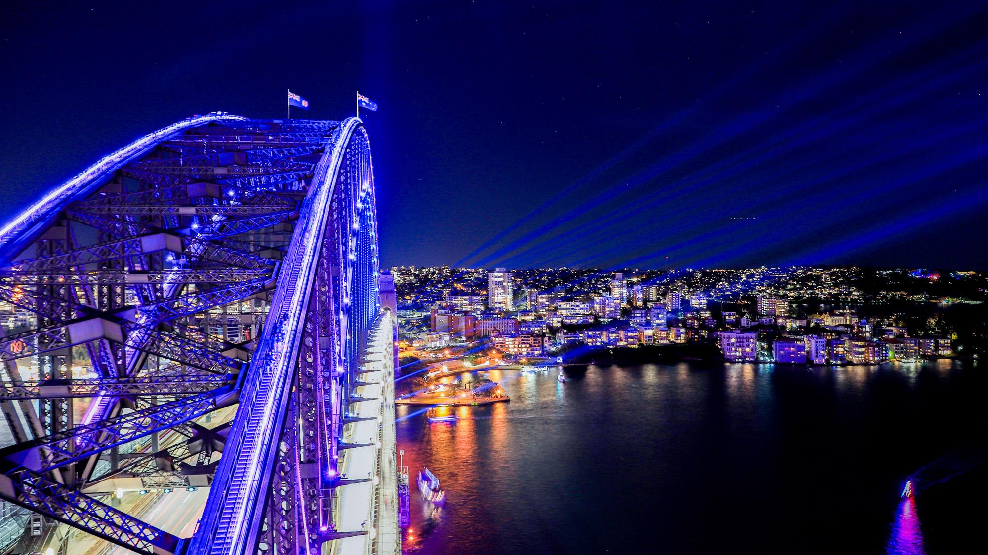 climbers walking along the iconic arches of the sydney harbour bridge with a view of the harbour, the sydney opera house and city skyline in the background